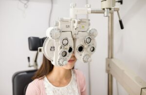 A woman sitting behind a phoropter in an optometrist's office