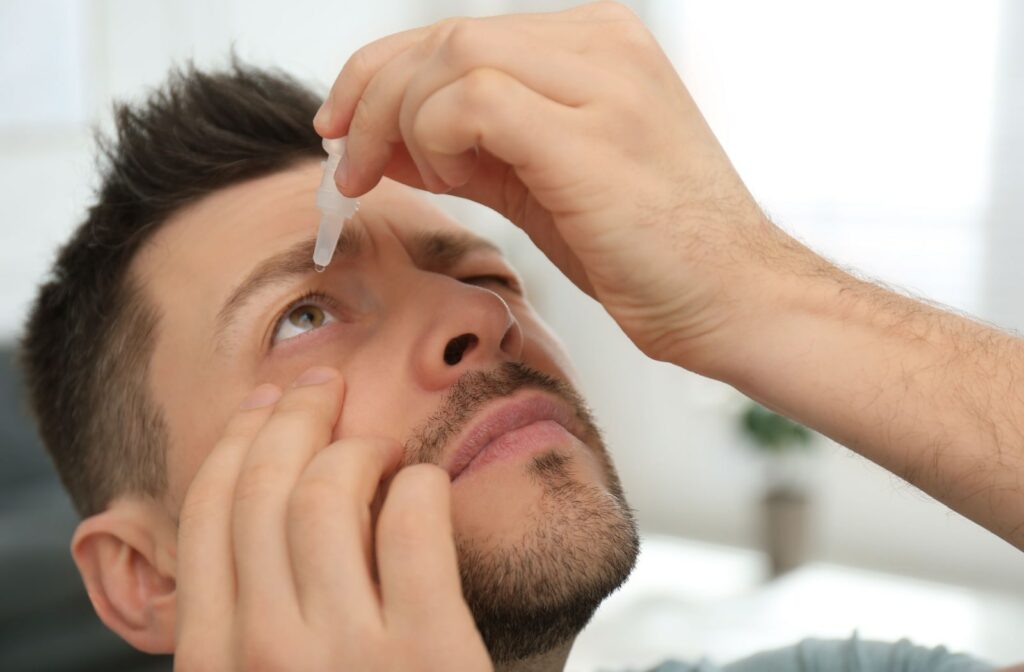 A close-up of a man applying eye drops to his right eye.