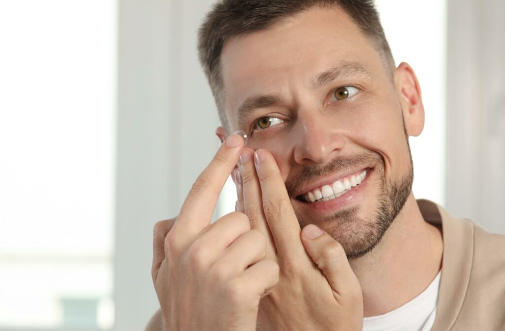A smiling man holds his lower eyelid as he prepares to insert a contact lens into his eye.