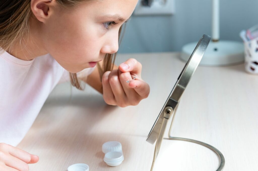 A young child leans into a mirror to put their contact lenses in.