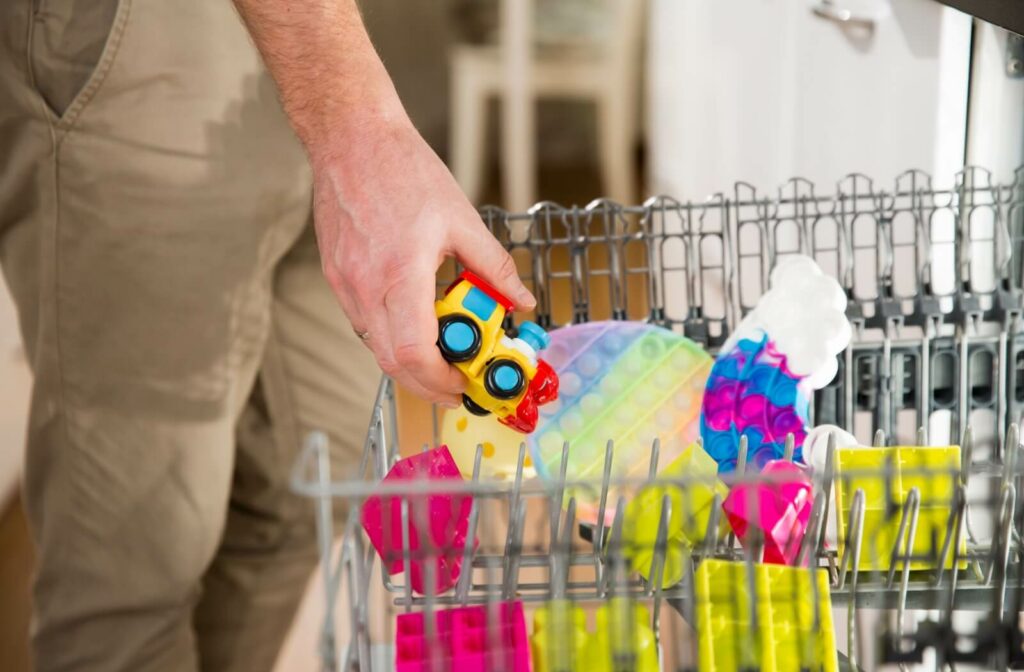 A parent places several children’s toys onto the upper rack of a dishwasher to clean them of lingering pink eye viruses.