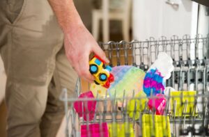 A parent places several children’s toys onto the upper rack of a dishwasher to clean them of lingering pink eye viruses.