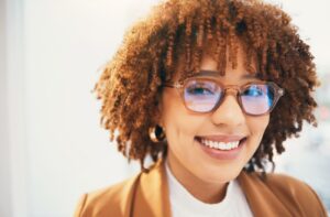 A headshot of a happy business professional smiling while wearing blue-lens eyeglasses.
