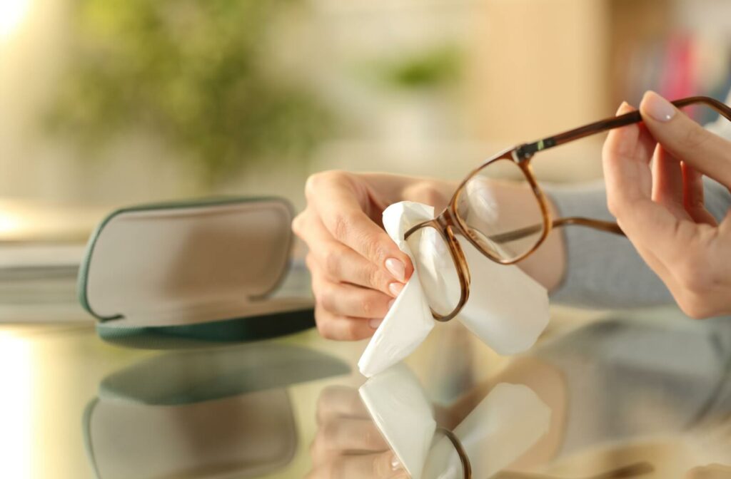 A person carefully cleans their eyeglasses with a microfibre cloth before storing them away in the lens case.