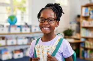 A cheerful kid wearing myopia eyeglasses smiles on their first day back to school.
