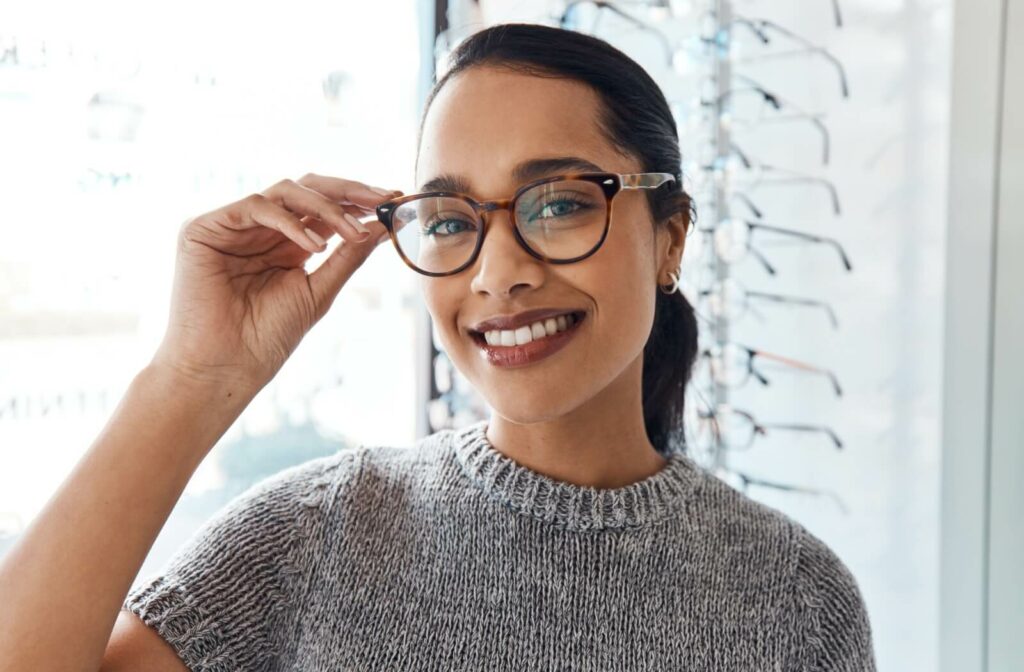 A person smiles widely as they try on the perfect pair of glasses for their face and style at their optometrist's office.
