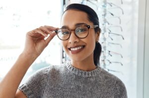 A person smiles widely as they try on the perfect pair of glasses for their face and style at their optometrist's office.