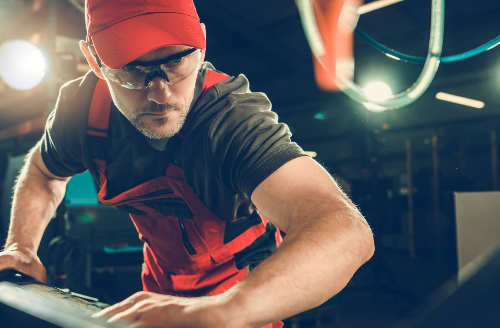 Industrial worker in safety glasses and protective gear focused on operating machinery in a workshop.