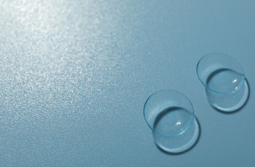 A close-up view of two clear contact lenses resting on a textured light blue surface, illustrating considerations for contact lens wear during allergy flare-ups.